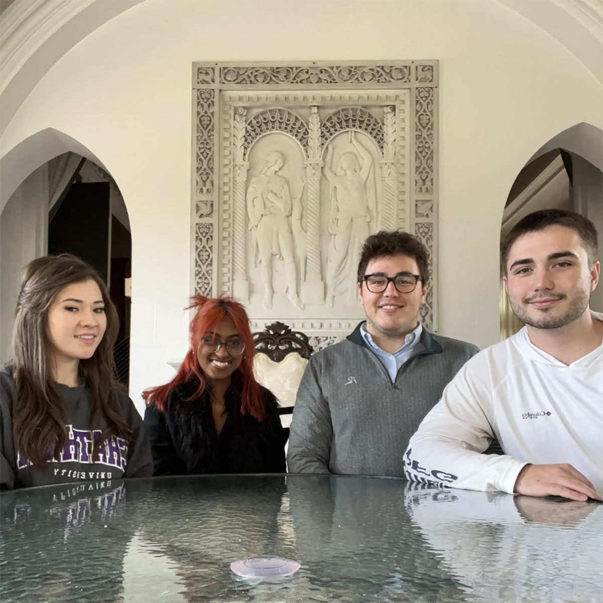 Photo of four students seated together at a table, smiling for the camera