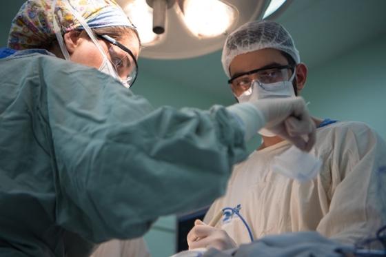 Two medical professionals work over an operating table together wearing scrubs, caps, and masks. 