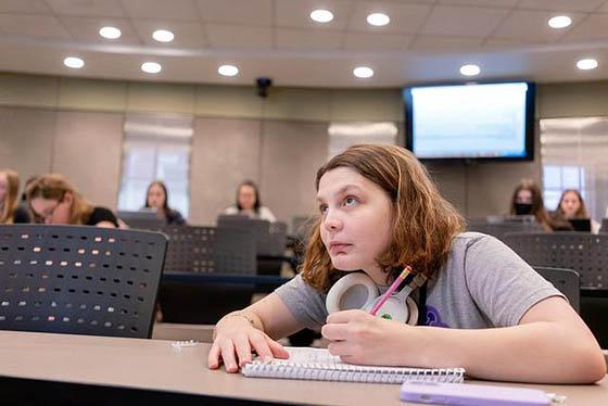 Photo of a student looking towards an instructor off screen in a lecture hall and taking notes